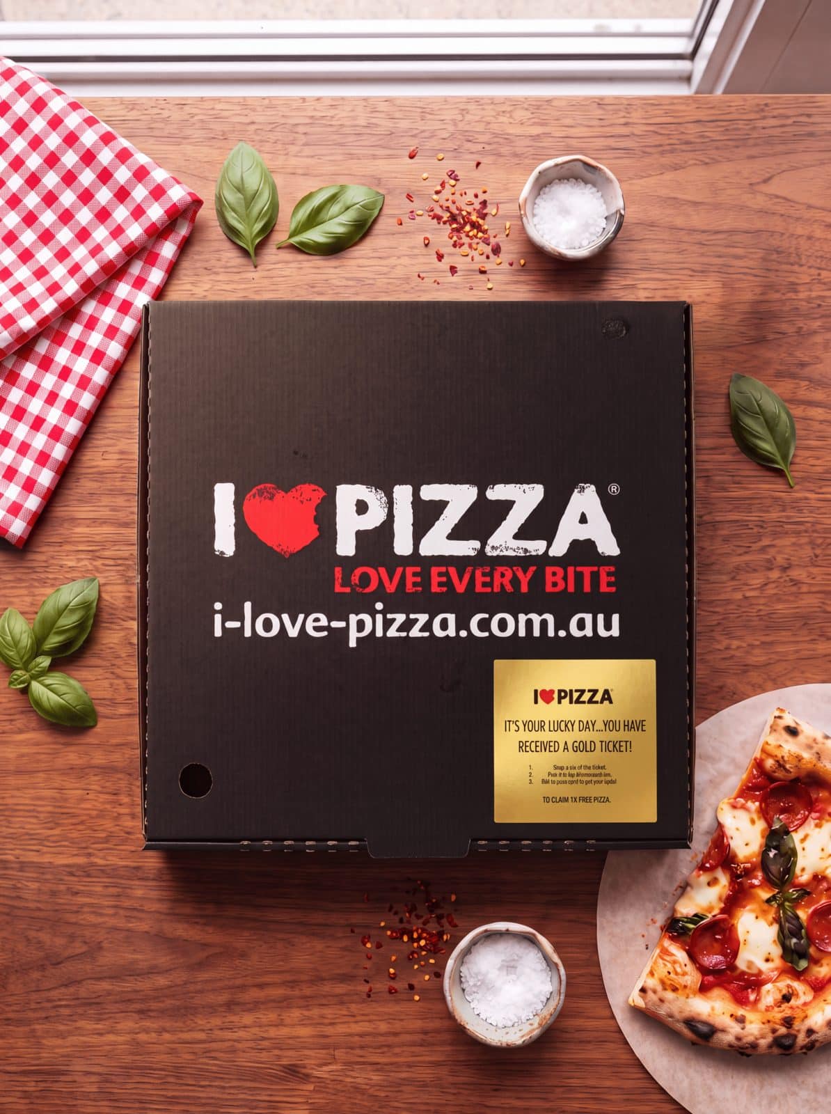 I Love Pizza box on a timber table with basil and a slice