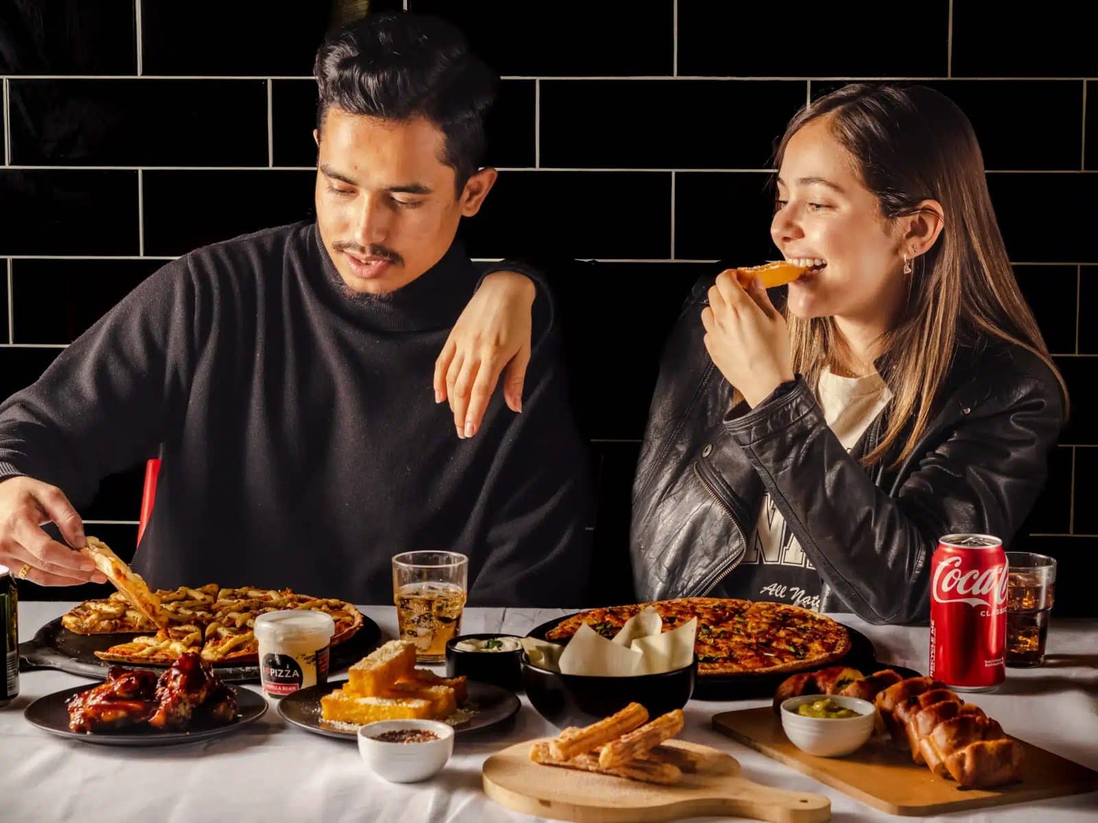 Two friends sharing pizza, wings and garlic bread at a table